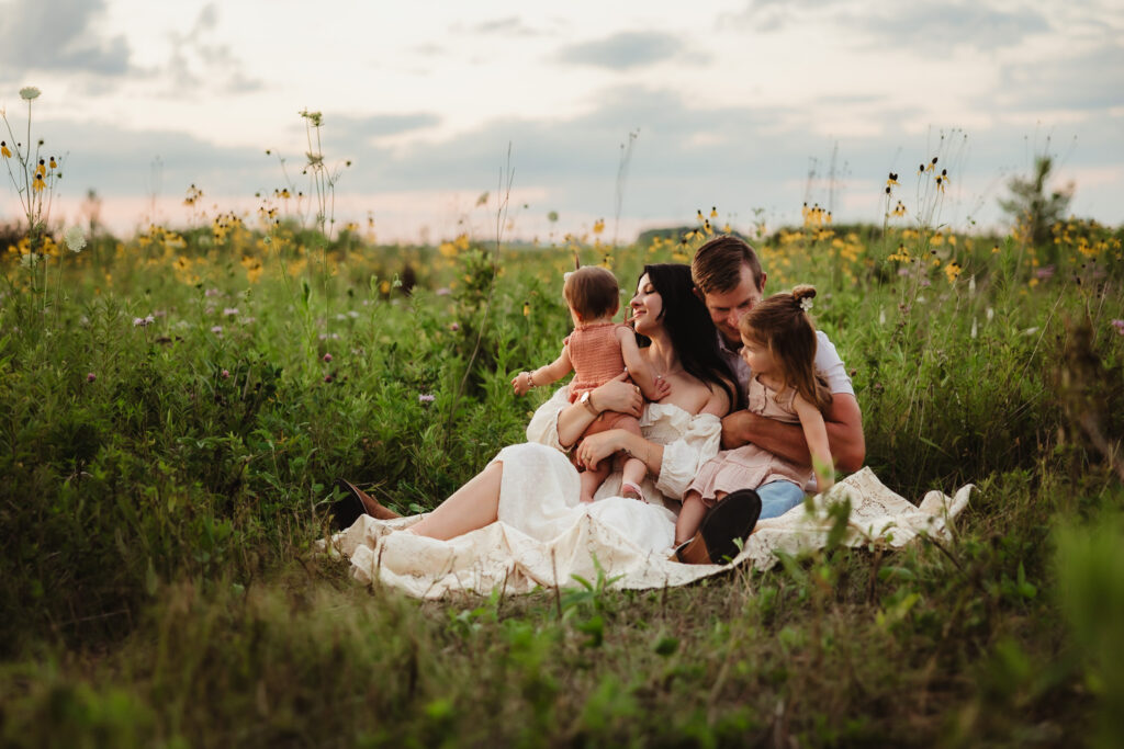 A family of four snuggles in a wildflower field during their summer outdoor family photos session.