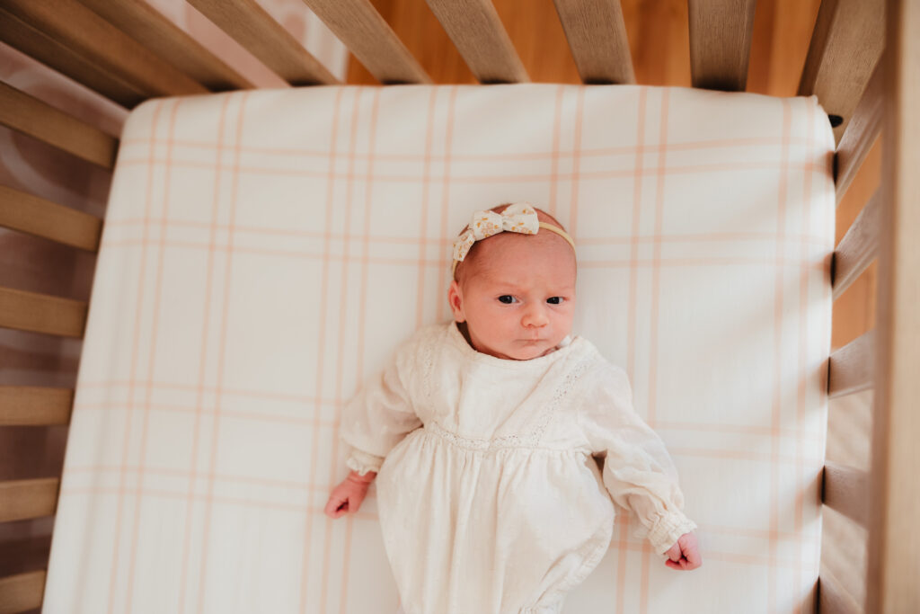 A newborn lays in her crib and makes eye contact with the camera during her lifestyle newborn photography session.