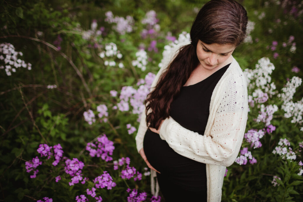 A pregnant mother holds her belly as she stands among the wild geraniums.