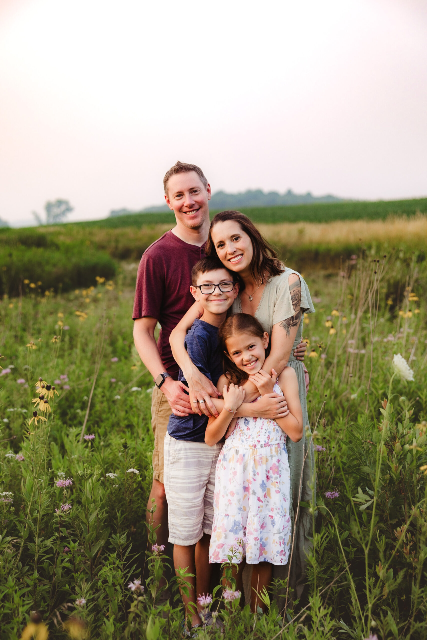A family of four stands and embraces each other while smiling at the camera during the family photo session in Madison WI.