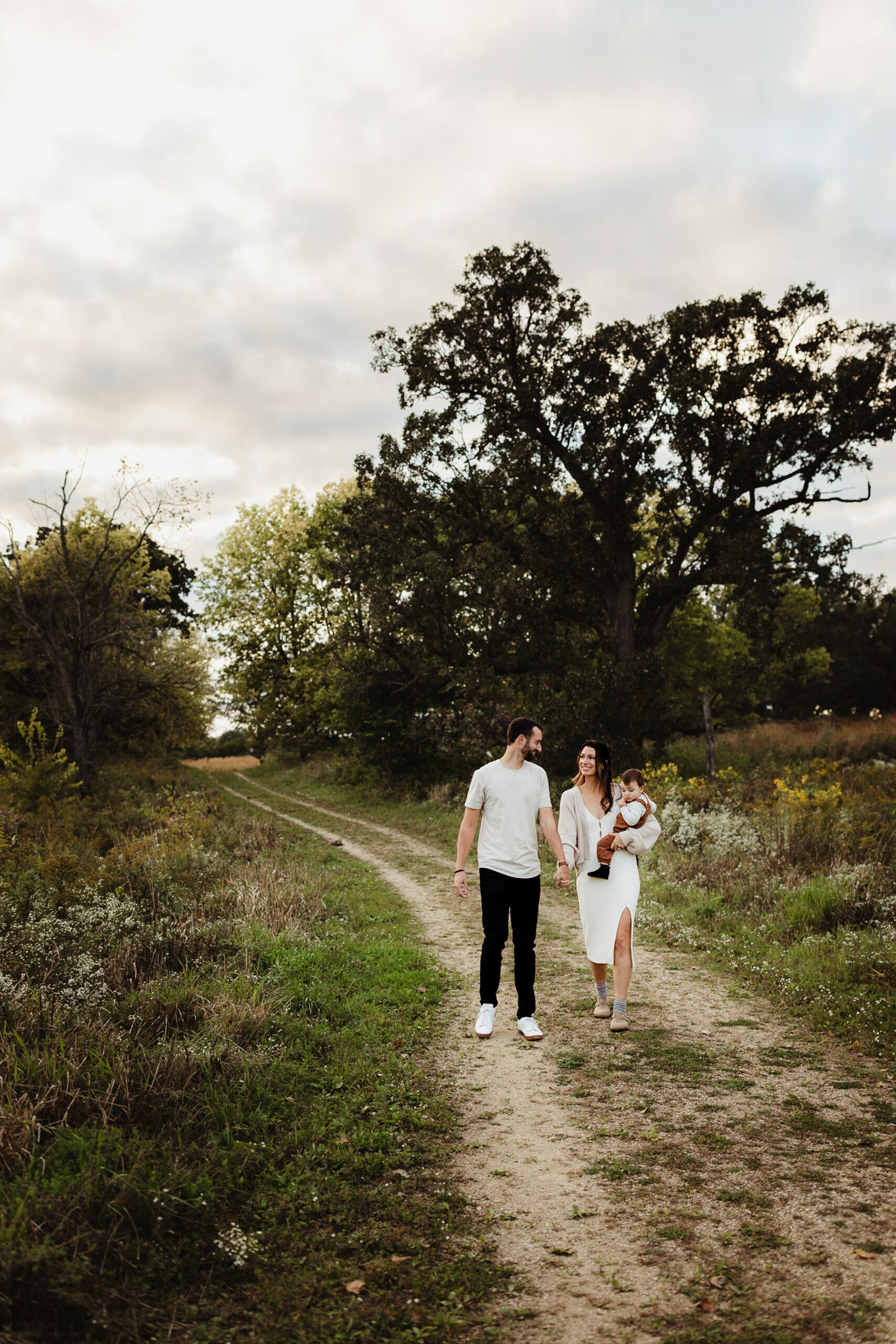 A young family of three strolls down an old worn nature path during their family photos session in Madison WI.