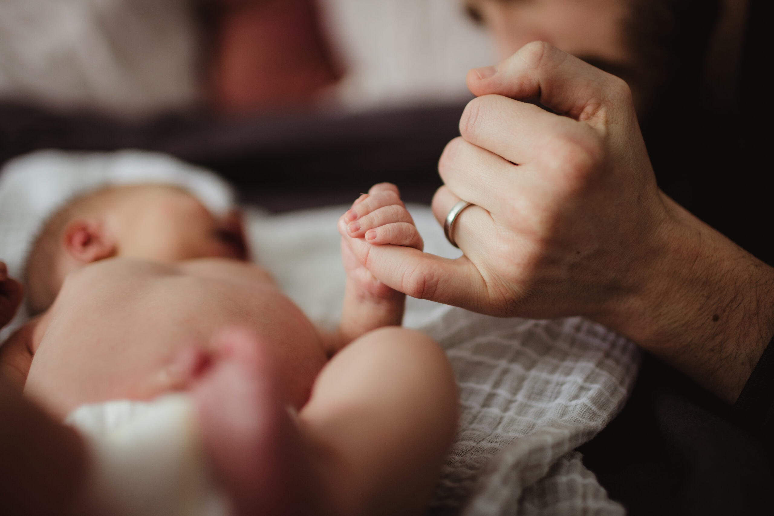 A newborn baby holds wraps his tiny fingers around his dads pinky after his Madison hospital birth.